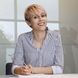 Jamie D'ath smiles at the camera while about to write on a document sitting on a table.