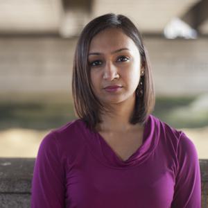 Roma Agrawal stares straight into the camera. She appears to be under a structure of some kind, perhaps a bridge.